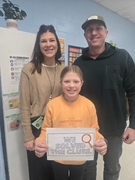 A man in a black Adidas hoodie and a woman in a tan sweater stand on either side of a girl in an orange "Abercrombie" sweatshirt. The girl is holding a sign with a magnifying glass that reads "WE SOLVED THE CLUES."