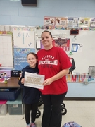 A woman in a red "Adventureland Iowa" t-shirt poses with a young girl in a dark hoodie and glasses. They are holding a sign that reads "WE CAME. WE SAW. WE ESCAPED." in a classroom decorated with "Rule" posters.