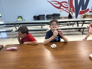 Two boys sitting side-by-side at a wooden cafeteria table smiling as they enjoy ice cream treats following the summer reading program.